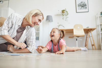 Young smiling women spending time with her daughter they laughing while lying on the floor and collecting puzzles at home