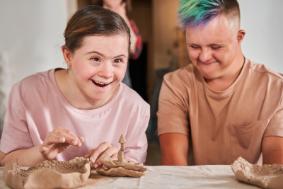 Waist up portrait view of the happy couple of the down syndrome people laughing out loud during the pottery master class