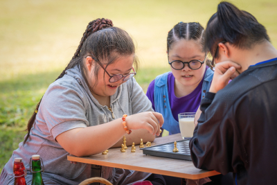 Group of friends with down syndrome having fun playng chess board together outdoor in park