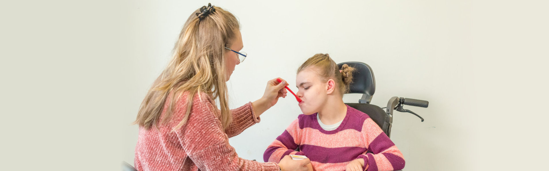 child in a wheelchair being cared for by a voluntary care worker who is helping with personal hygiene